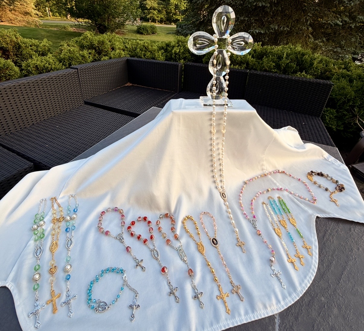 Outdoor table display of the full collection of handmade rosaries and bracelets under a crystal cross